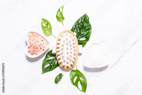 Spa and wellness concept. Eco friendly zero waste composition with cosmetic products and massage brushes on white marble background with green monstera leaves.