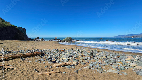 a beautiful spring landscape at Mile Rock Beach with blue ocean water, waves, rocks and lush green trees on Lands End Trail at Golden Gate National Recreation Area in San Francisco California USA