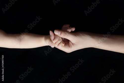 A mother's hand holds a child's hand on a black background. Details of the body - hands. Photo of newborns