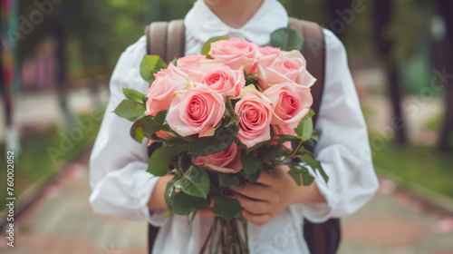 A schoolboy in a white shirt and with a backpack goes to school with a bouquet of pink roses to congratulate his teacher on Teacher's Day. The beginning of the school year is the first of September.
