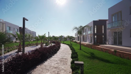 Modern luxury villas line landscaped walkway in upscale residential complex. Property investment options showcased in sunny setting. photo