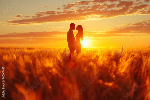 A couple is standing in a field of wheat at sunset. The sun is low in the sky, and the couple is silhouetted. The field is golden with the sunlight