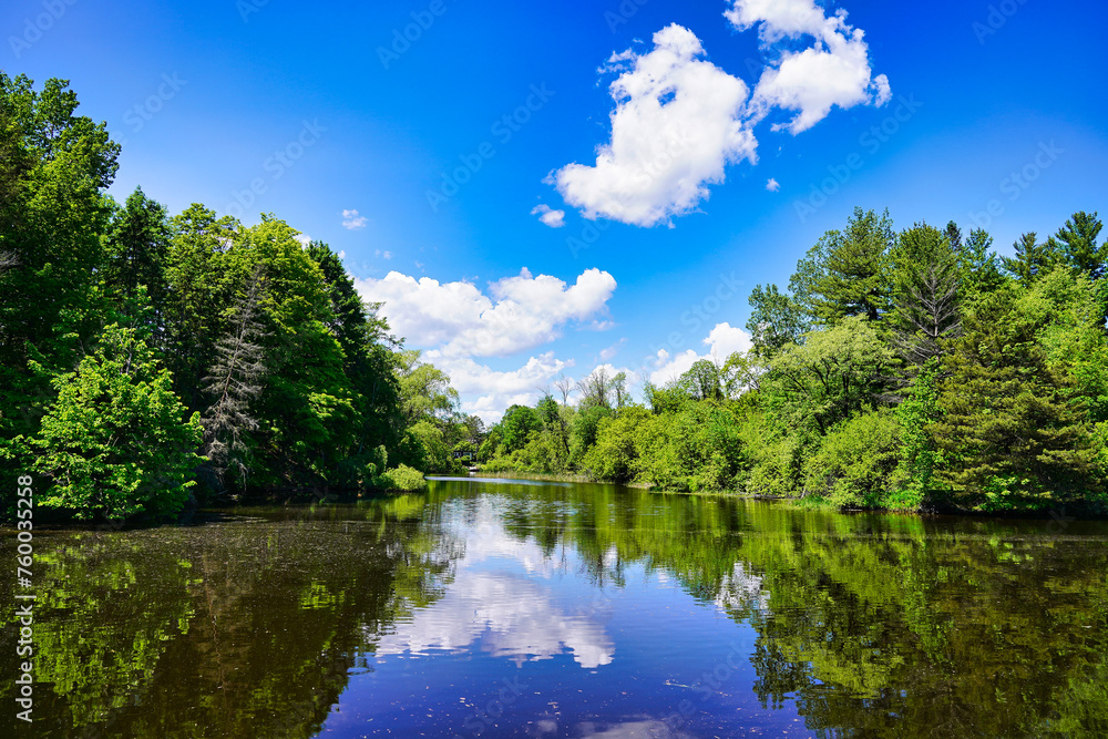Bright Summer day with greenery,trees and fluffy clouds in a blue sky reflected in the waters of the rideau canal at Ottawa,Ontario,Canada