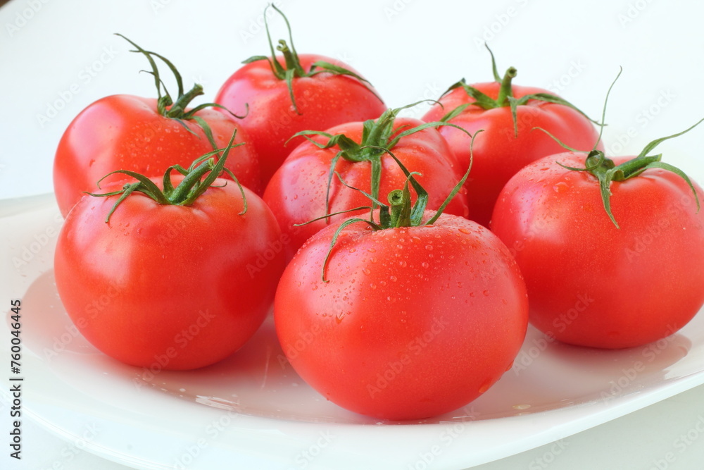 Lots of fresh ripe red tomatoes covered with water drops on a white background. Isolated. Close-up.