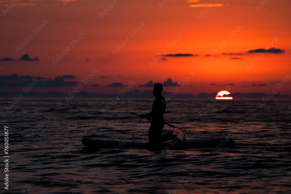 A man swimming in a boat in the sea at a beautiful red sunset