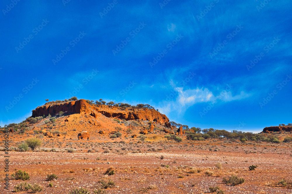 Red laterite (rocks with iron and aluminium) formations surrounded by saltbush and mulga in the desert near Mount Magnet, Western Australia.
