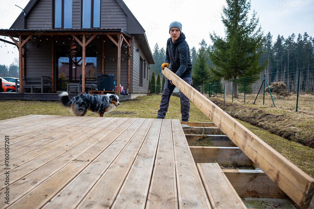 Man working on a deck or terrace  with his loyal dog companion in the yard of a countryside home