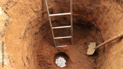 water at the bottom of a newly dug well, top view, in the well, a digger's tool, a shovel and a ladder