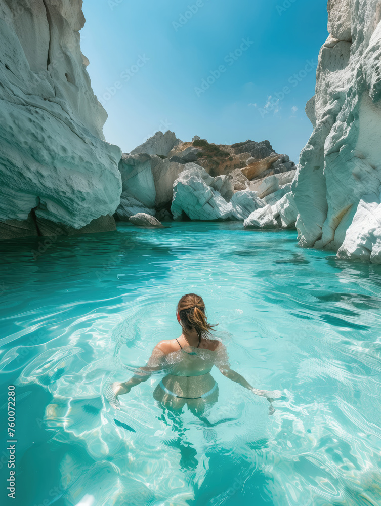 A solitary swimmer enjoys the stunning clarity of a turquoise lagoon flanked by white rocky cliffs under a clear blue sky.