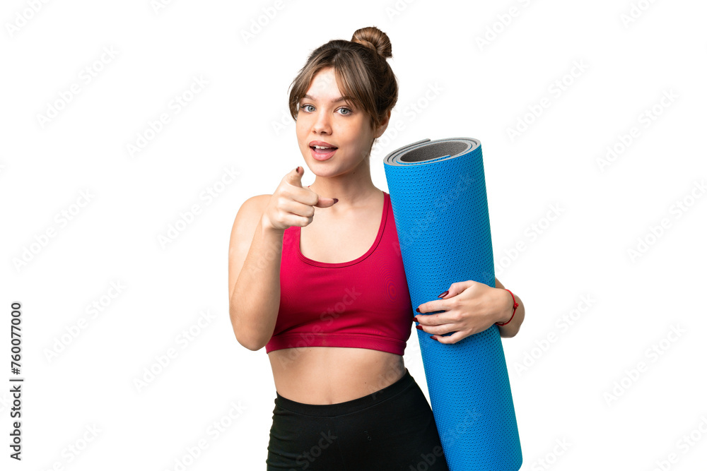 Young sport girl going to yoga classes while holding a mat over isolated chroma key background surprised and pointing front