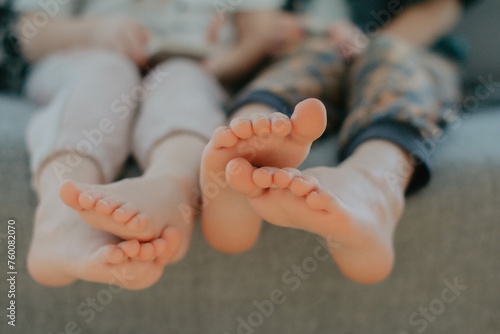 Big brother and little sister holding bare feet close up to camera . Blurred face on background 