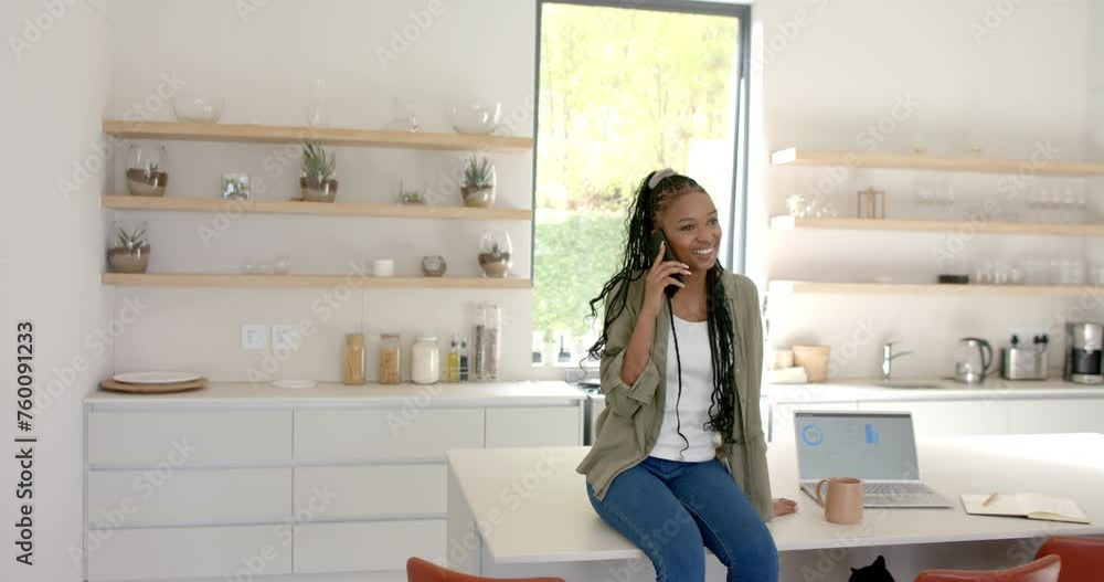 A young African American woman is chatting on her smartphone with copy space in a kitchen at home A young African American woman is chatting on her smartphone with copy space in a kitchen at home