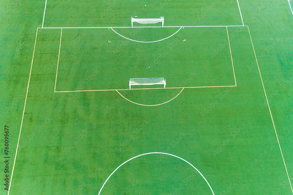 A soccer field with two goals and a bench. The field is green and well maintained. Aerial drone view