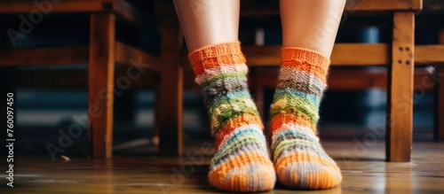 A person is seated on a wooden chair with colorful socks. Their foot is resting on the flooring, showing off their unique sock design