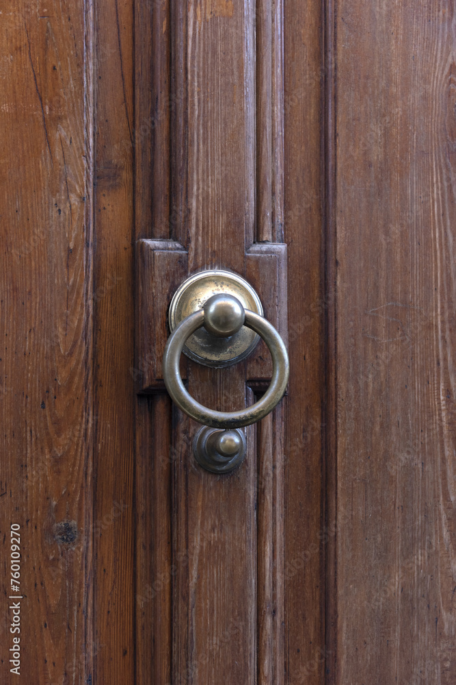 Round metal bronze door handle on a wooden front door in a European city, vertical view, street photo Round metal bronze door handle on a wooden front door in a European city, vertical view, street photo