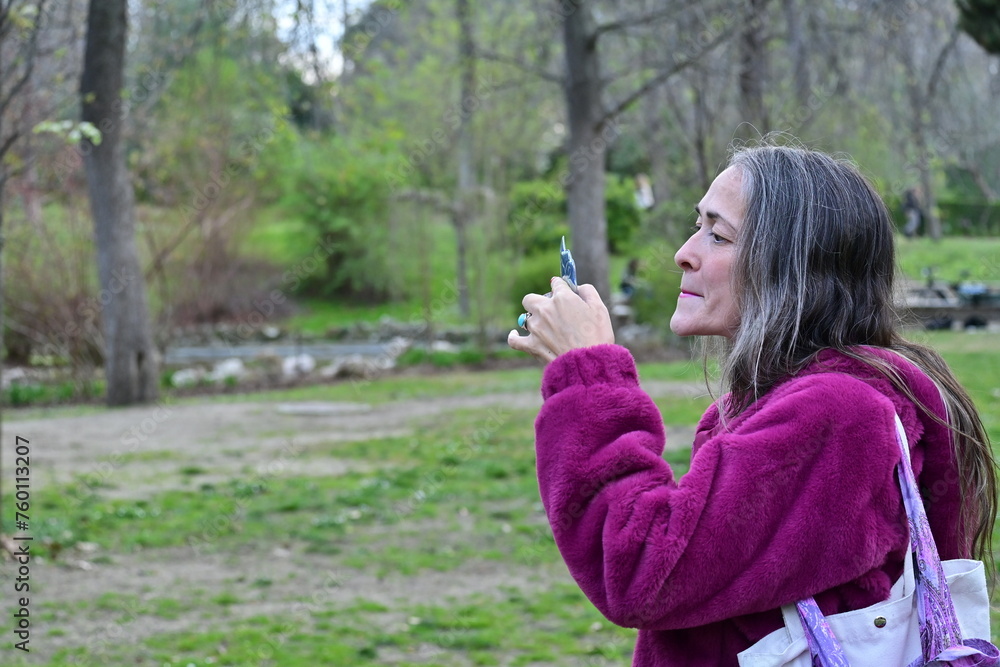 Woman applying her make-up while walking in a park Woman applying her make-up while walking in a park