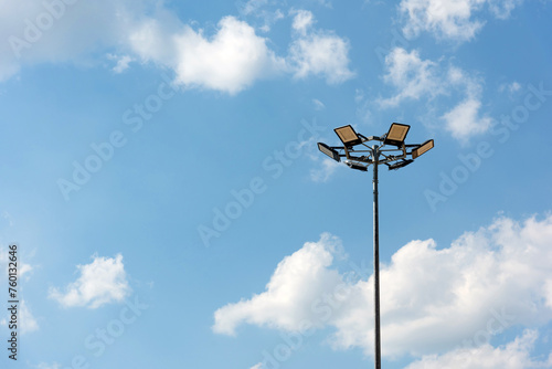 Tall metal lamppost with lamps in a circle against a blue cloudy sky - street lighting, LED lamps, energy saving