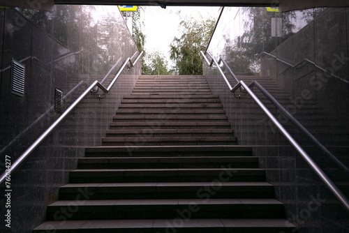 A wide stone staircase with iron railings rises to the top, exit from the subway, steps lead to the street, come out of the ground, granite cladding photo