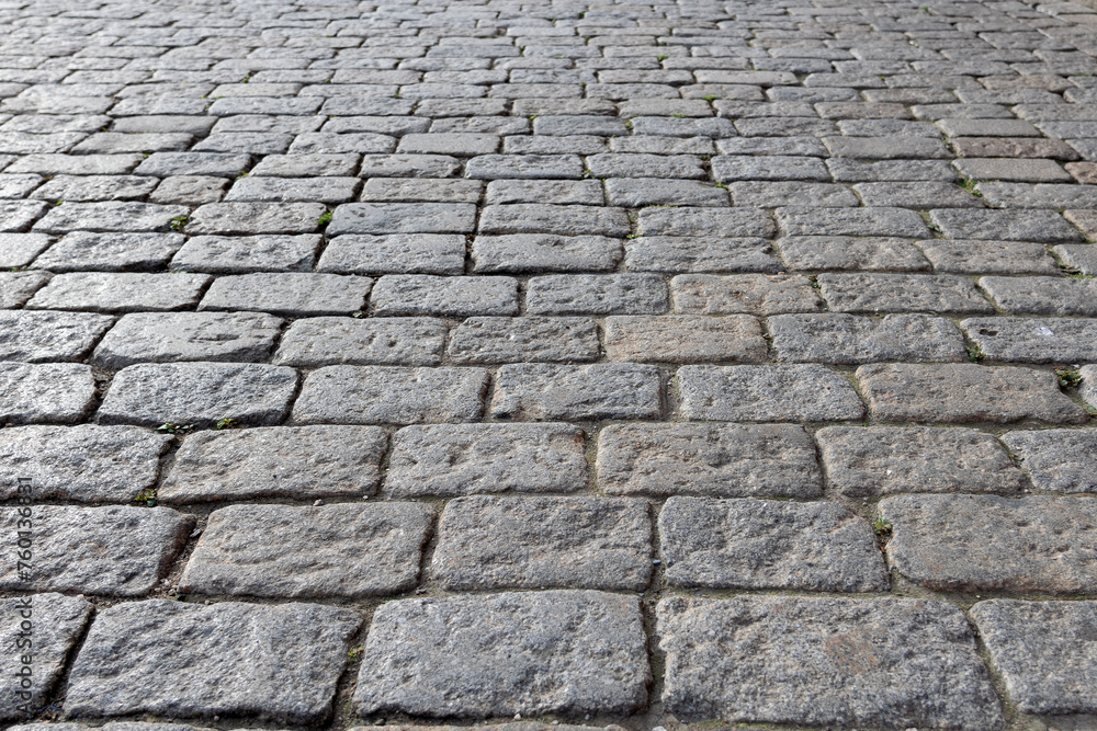 City square street lined with square gray bricks, cobblestones, city pavement all over the square to the horizon - close-up, blurred background