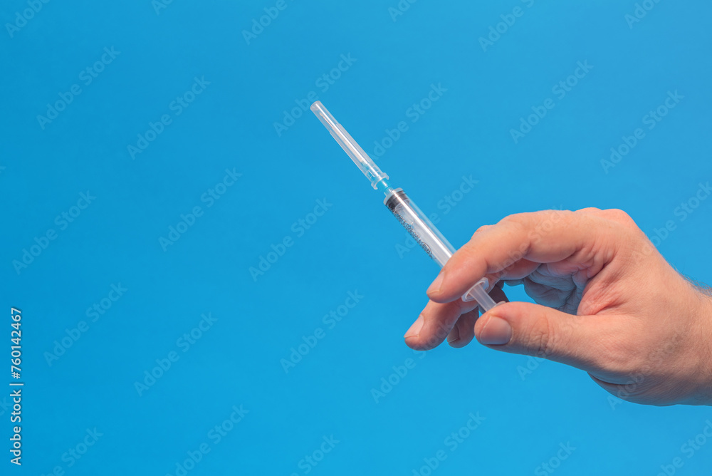 A man holds a medical disposable syringe in his hand, on a blue background A man holds a medical disposable syringe in his hand, on a blue background