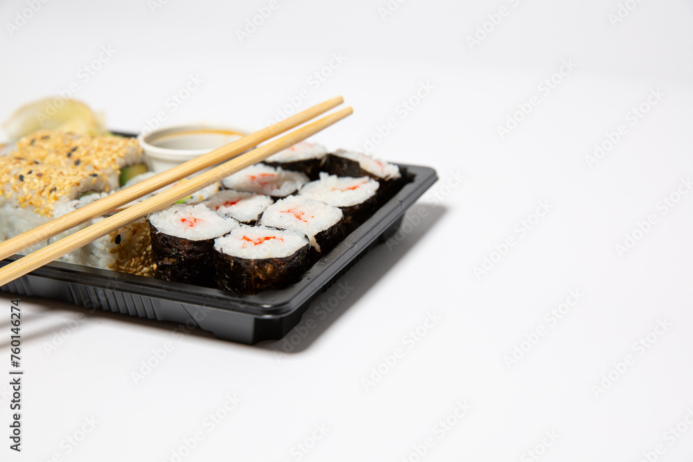 Sushi to go in a black takeaway box with wooden chopsticks on white background Sushi to go in a black takeaway box with wooden chopsticks on white background