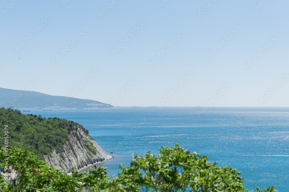 Landscape of the blue sea with a green high coast against the blue sky on a sunny day