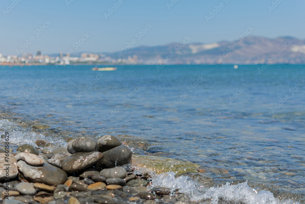 Seascape - wet round pebbles in the foreground are covered with a wave of the blue sea, mountain hills are visible in the distance on the horizon