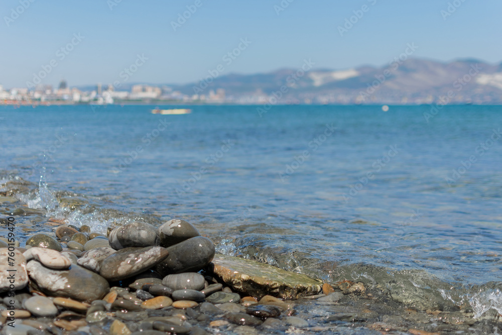 Seascape - wet round pebbles in the foreground are covered with a wave of the blue sea, mountain hills are visible in the distance on the horizon
