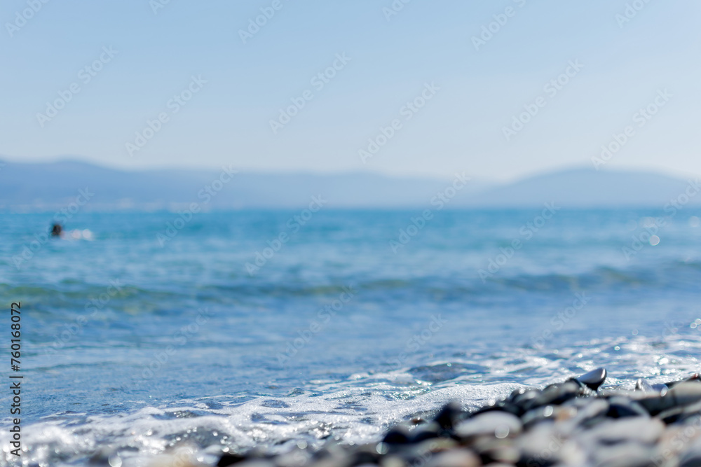 Seascape - sea waves crash into white foam on a rocky shore, boats float far out to sea, blue water merges with high mountains on the horizon