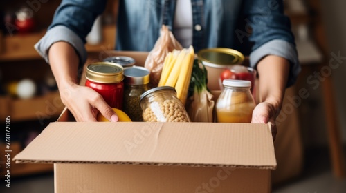 Caring hands preparing a cardboard box filled with various preserved and fresh food items for donation photo