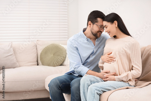 Happy pregnant woman with her husband on sofa at home, space for text