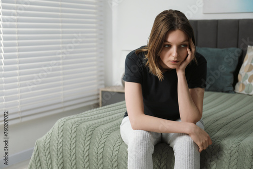 Sad young woman sitting on bed at home, space for text