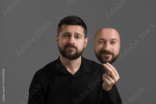 Man holding mask with his facial expression on grey background. Personality crisis, different emotions