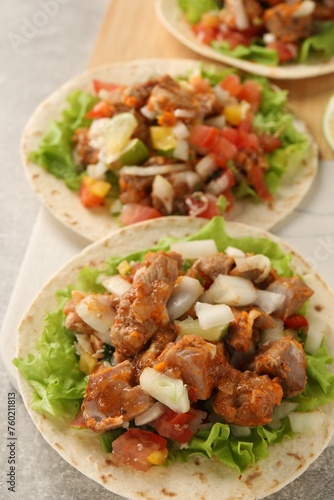 Delicious tacos with vegetables and meat on light table, closeup