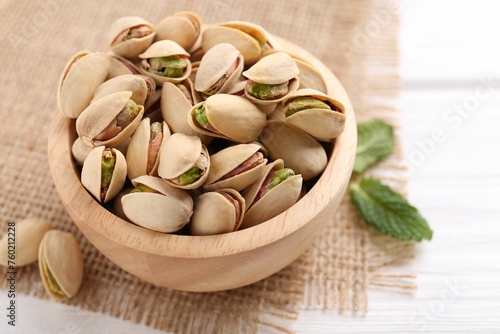 Tasty pistachios in bowl on white wooden table, closeup