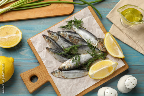 Fresh raw sprats, dill, oil and cut lemon on light blue wooden table, flat lay
