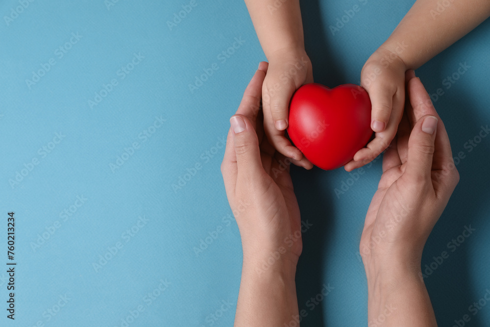 Mother and her child holding red decorative heart on light blue background, top view. Space for text Mother and her child holding red decorative heart on light blue background, top view. Space for text