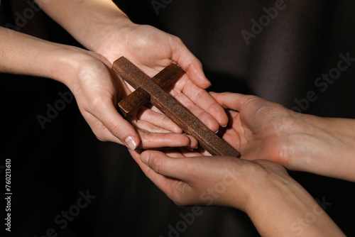 Easter - celebration of Jesus resurrection. Women holding wooden cross on dark background, closeup