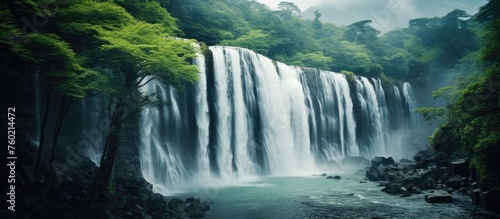 Serene Waterfall Cascading Through Lush Green Forest Landscape in Harmony with Nature © Ilgun