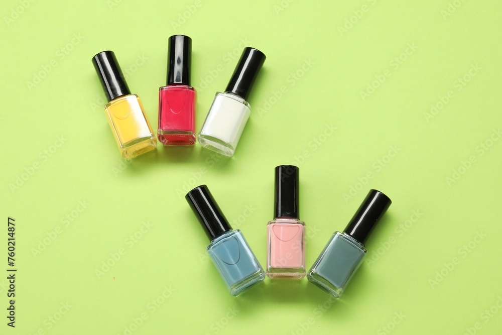Colorful nail polishes in bottles on green background, flat lay Colorful nail polishes in bottles on green background, flat lay