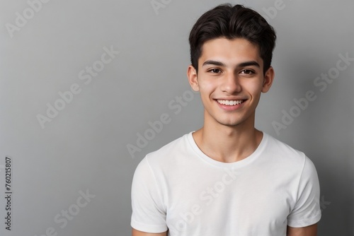 Young Brazilian man in a white shirt, smiling and looking at the camera, standing on a grey background with copy space. © PNG&Background Image