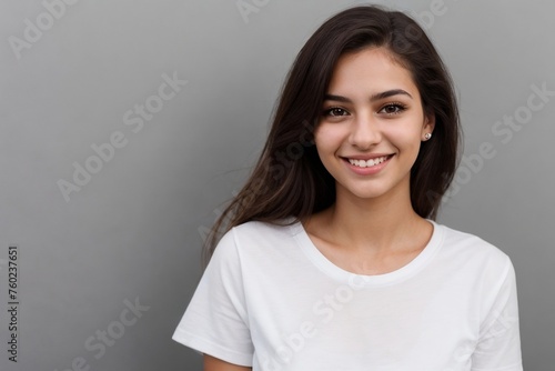 Young Brazilian woman in a white shirt, smiling and looking at the camera, standing on a grey background with copy space.
