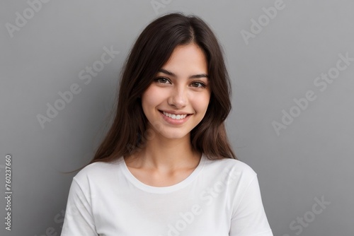 Young Brazilian woman in a white shirt, smiling and looking at the camera, standing on a grey background with copy space.