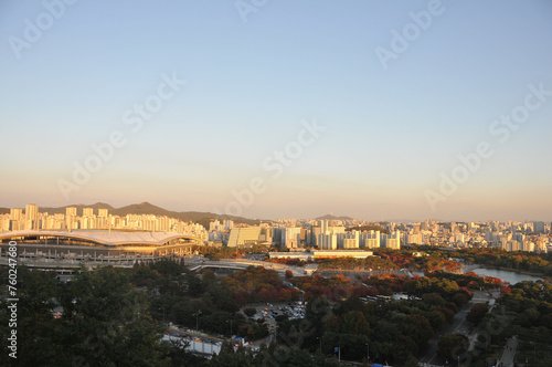 SEOUL, SOUTH KOREA - OCTOBER 24, 2022: Colourful foliage trees in Autumn with Han river, World Cup stadium, and skyscraper buildings in the afternoon and blue sky.