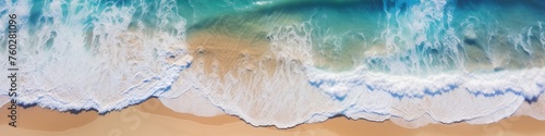 Aerial view of a paradise beach where the waves of the sea break on the shore. Top view of a sandy coast with turquoise blue water and white foam on sunny day. Summertime, marine, seashore banner. 