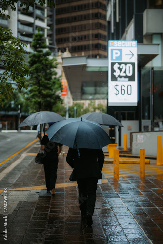 3 people walking with umbrellas up a city street