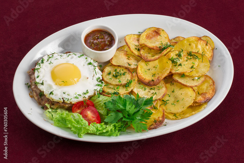 Delicious meat cutlet with egg with a side dish in the form of fried potatoes on a plate, menu for a restaurant
