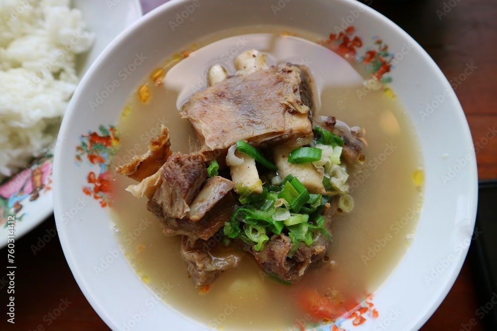 Sop Iga Sapi in white bowl on the wooden table. Beef Rib Soup is typical Indonesian dish, made from mixing beef ribs, carrots, leeks and celery. Selective focus.