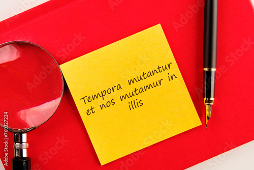 Tempora mutantur et nos mutamur in illis Translated from Latin, it means Times are changing, and we are changing with them. on a yellow sticker on a red notebook photo