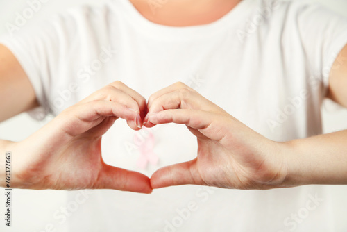 Woman with pink ribbon on t-shirt and showing heart by hands. Cancer concept.